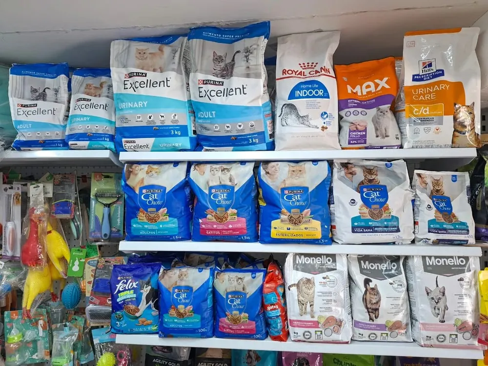 Estantería de comida para gatos en Patitas Pet Shop con bolsas de Excellent, Royal Canin, Max, Cat Chow, Whiskas y Monello, y juguetes al fondo